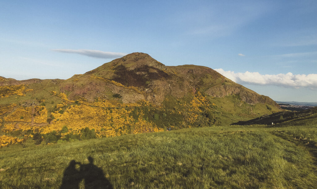 arthurs seat in edinburgh from a distance with two shadow figures in the frame